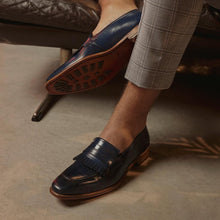 Load image into Gallery viewer, Casual setting with a model wearing the navy fringe penny loafers, paired with light grey trousers, illustrating the shoe's versatility and elegance.