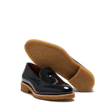 Load image into Gallery viewer, Angled view of patent black Belgian loafers with the crepe sole lifted to display the caramel-colored bottom.