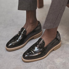 Load image into Gallery viewer, A lifestyle shot of a person wearing patent black Belgian loafers with grey trousers, demonstrating the shoe's elegance for smart casual attire.