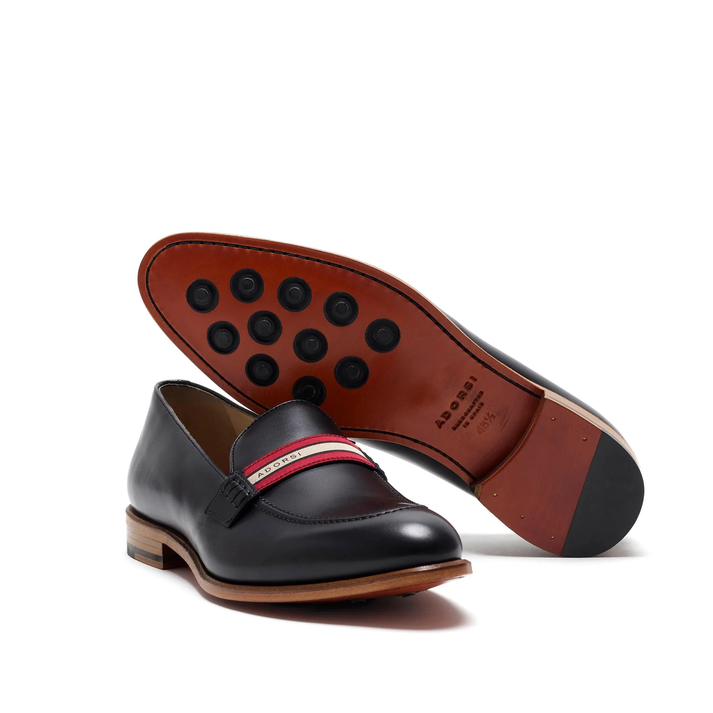 Unique underside view of a black calf loafer with a web stripe, displaying the rubber grommets on a leather sole, taken on a clear white setting.