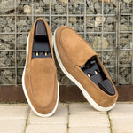 Camel suede casual loafers with wooden shoe stretchers inside, casually placed against a textured urban background, accentuating the loafers’ versatile style.
