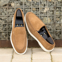 Load image into Gallery viewer, Camel suede casual loafers with wooden shoe stretchers inside, casually placed against a textured urban background, accentuating the loafers’ versatile style.

