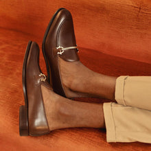 Load image into Gallery viewer, Lifestyle image featuring a person wearing dark brown calf leather horsebit loafers, paired with beige trousers, capturing the footwear&#39;s versatility and classic style.
