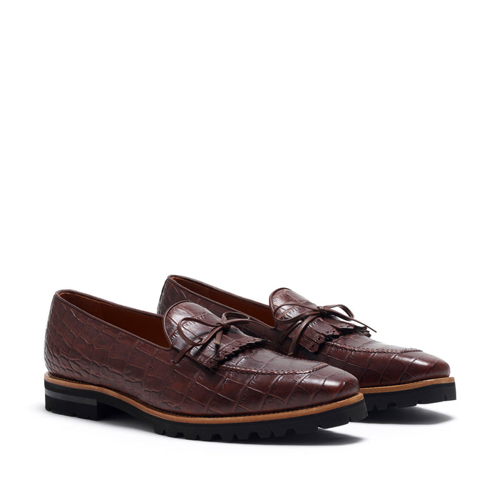 Front view of dark brown painted croco laced kiltie loafers showcasing the intricate texture and detailed bow-tie lacing on a white background.