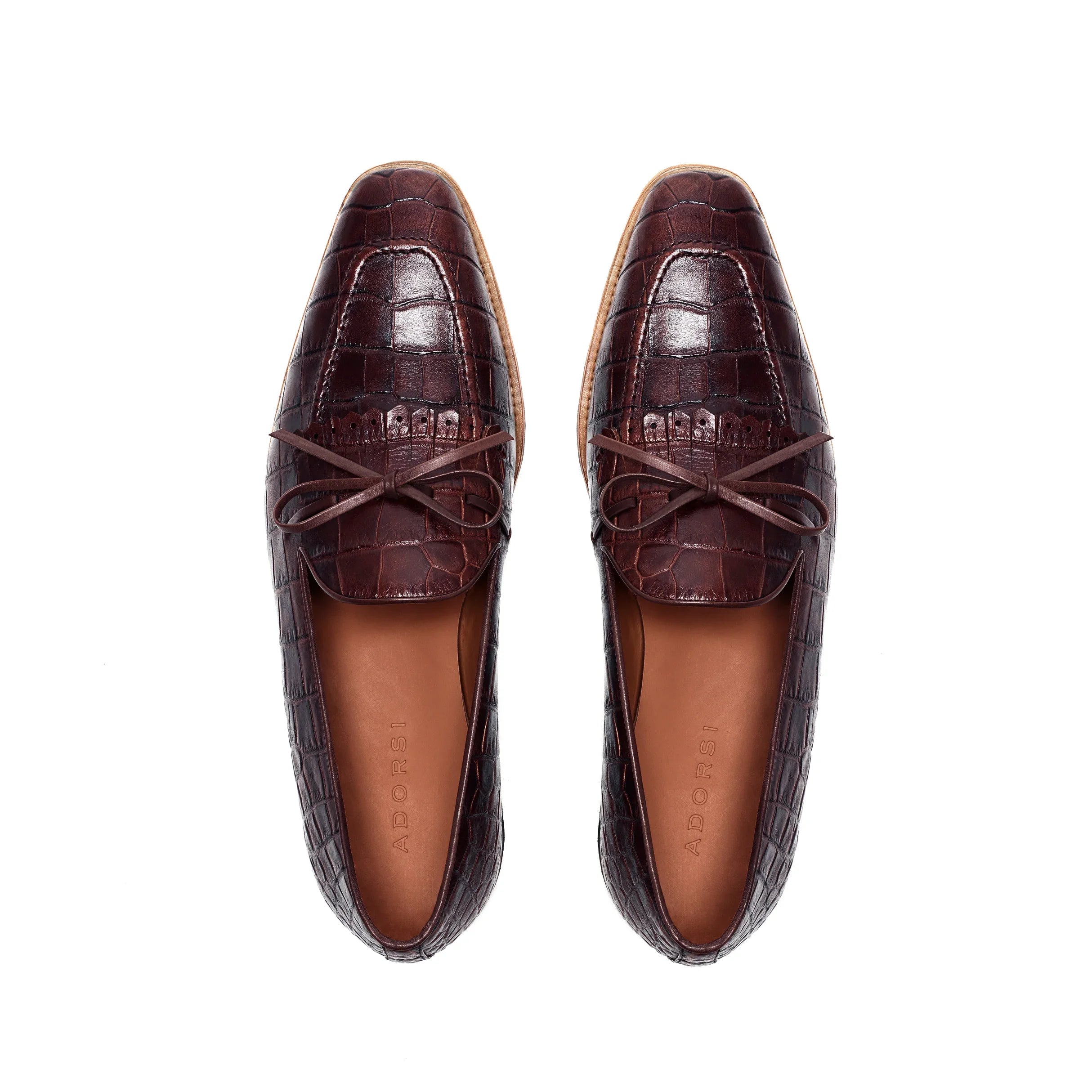 Top-down image of dark brown kiltie loafers, emphasizing the painted crocodile texture and neat lacing, against a pristine white surface.