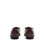 Rear angle showcasing the back detail of dark brown croco-textured kiltie loafers, set against a white environment.