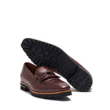 Angled perspective of dark brown kiltie loafers with a visible sturdy black chunky commando sole pattern, highlighting durability and design, against a white stage
