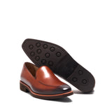 Underside view of a burnished medium brown calf plain loafer with a brown rubber sole featuring circular grips, displayed on a white setting.