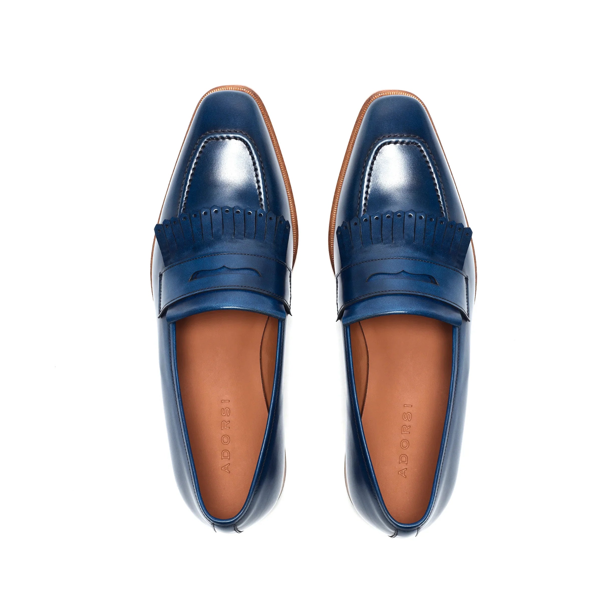 Overhead view of navy blue penny loafers with fringe, revealing the meticulous stitching and the classic penny slot on a white surface.