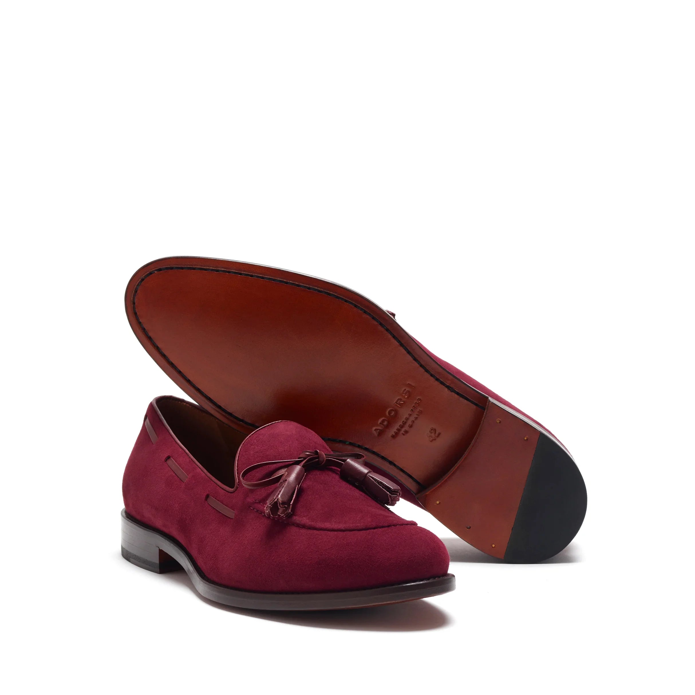 Angled shot presenting the wine suede loafer's profile with its burgundy leather laced tassels, cognac leather sole, alongside the shoe's profile, capturing the harmony of form and function.